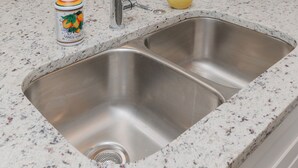 Una cocina con un lavamanos de acero inoxidable, encimera de mármol, una planta en maceta y un reloj de pared.