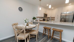 Una cocina moderna con armarios blancos, un refrigerador de acero inoxidable y una mesa de comedor de madera con sillas.