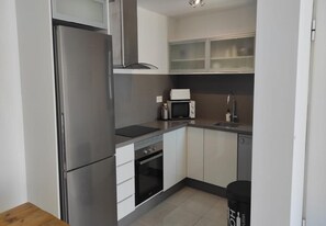 A compact kitchen with a refrigerator, microwave, oven, and a sink.