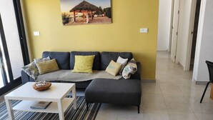 A living room with a sofa, ottoman, and a coffee table. There is a painting on the wall and a window with blinds. - Apartment  Vitamina & Sea, Mil Palmeras, Torre de la Horadada (Torre de la Horadada)