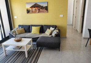 A living room with a sofa, ottoman, and a coffee table. There is a painting on the wall and a window with blinds.