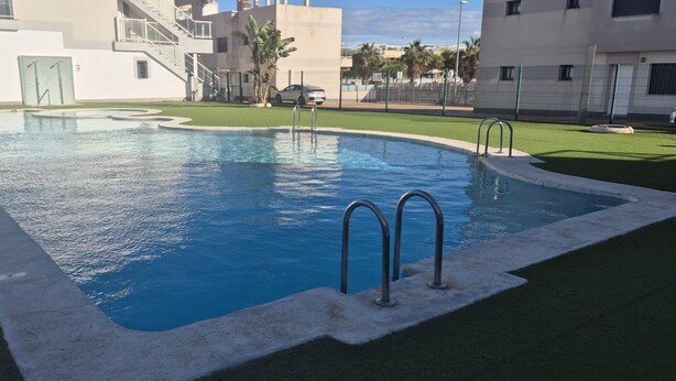 A swimming pool with a clear blue water, surrounded by artificial grass and concrete edges. - Apartment  Vitamina & Sea, Mil Palmeras, Torre de la Horadada (Torre de la Horadada)