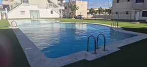 Una piscina con agua cristalina azul, rodeada de césped artificial y bordes de concreto.