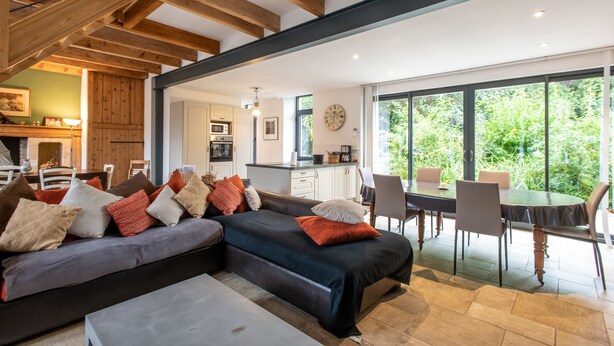 En moderne stue med sofa, spisebord og et køkken i baggrunden.