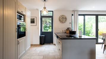 Une cuisine moderne dotée d’appareils électroménagers intégrés, d’un grand îlot central et offrant une vue sur l’extérieur grâce à une porte vitrée.