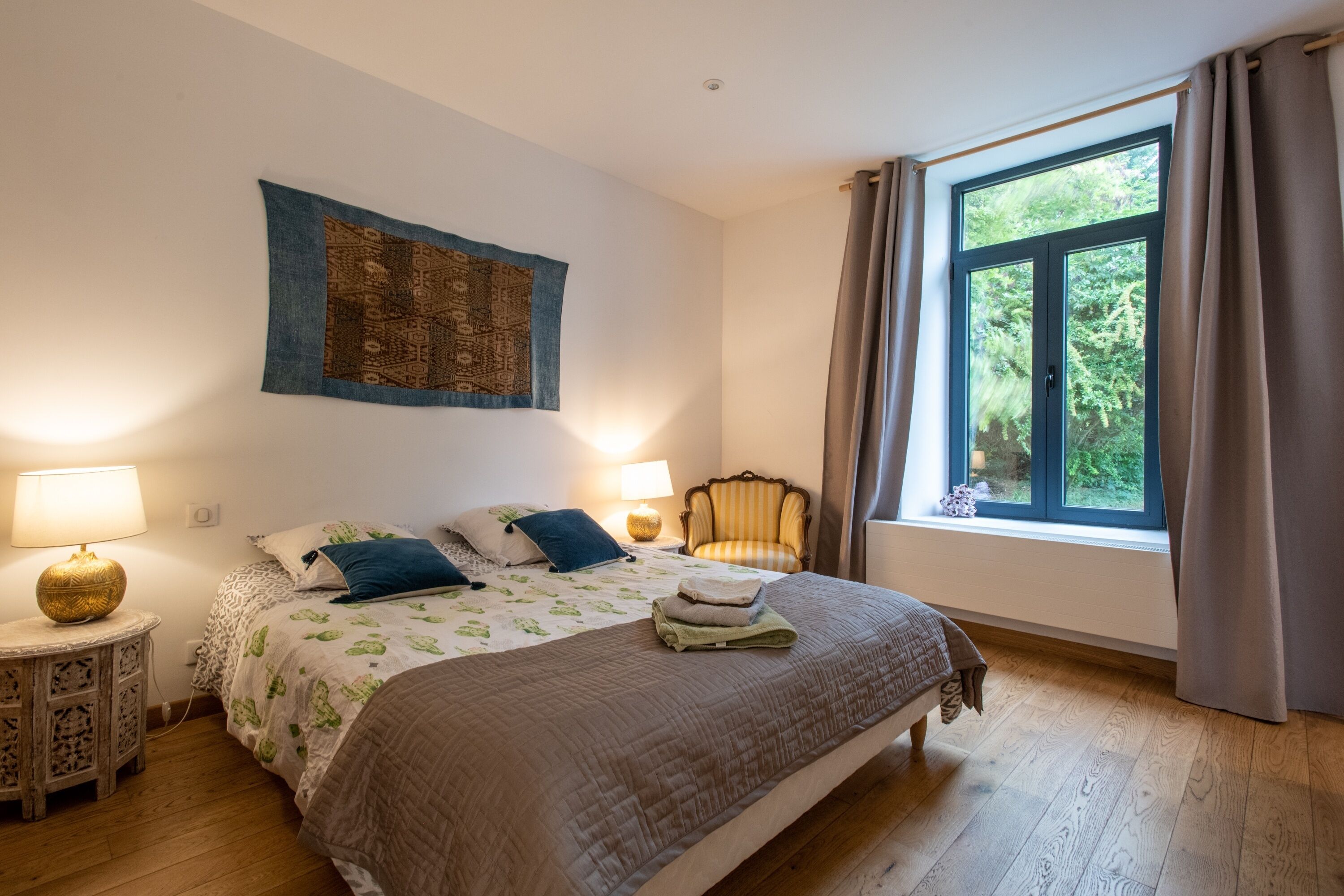 Une chambre à coucher avec un grand lit, deux lampes de chevet, une chaise et une fenêtre avec des rideaux.