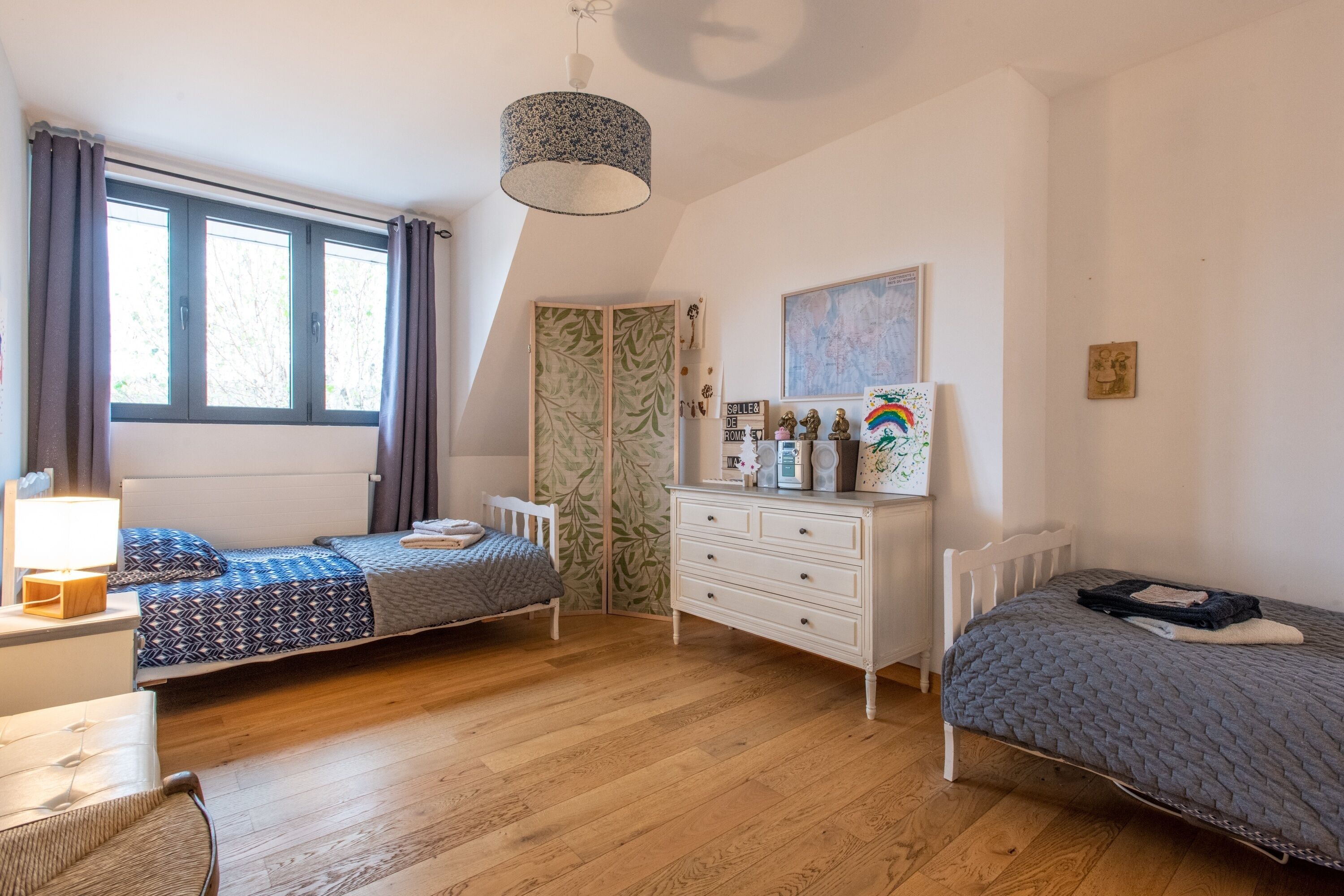 A bedroom with two single beds, a dresser, a wardrobe, and a desk with a lamp.
