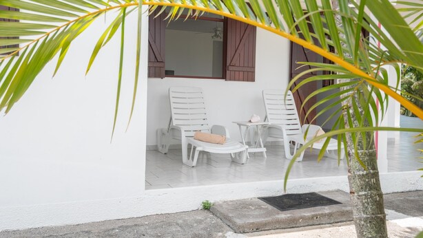 Een wit gebouw met een overdekte patio, voorzien van witte plastic stoelen en een kleine tafel.