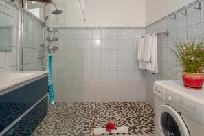 A bathroom with a shower, a bathtub, a washing machine, and a tiled floor. - La Résidence Anhiel - Maison Climatisée (Sainte-Anne)