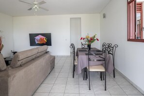 A dining area with a table set for four, a sofa, a ceiling fan, and a framed picture on the wall. - La Résidence Anhiel - Maison Climatisée (Sainte-Anne)