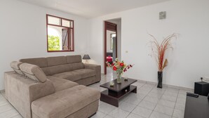 Een moderne woonkamer met een hoekbank, een salontafel met bloemen, een lamp en een tv-meubel.