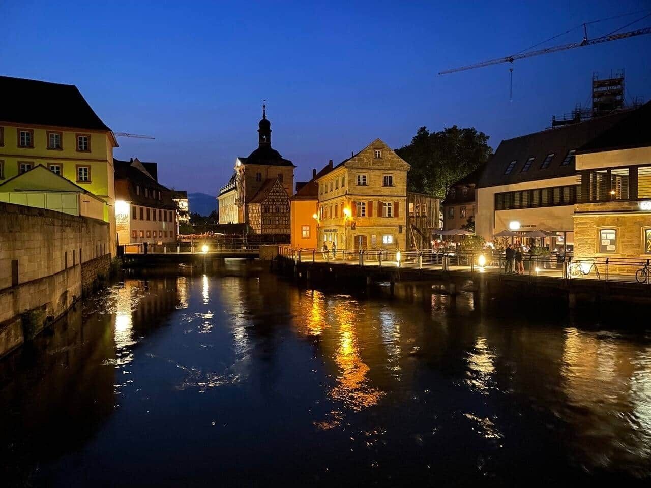 A canal with buildings on either side, including a church with a steeple and a brightly lit building with a sign.