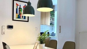 Een moderne eethoek met een witte tafel, twee zwarte hanglampen en een ingelijste foto aan de muur.