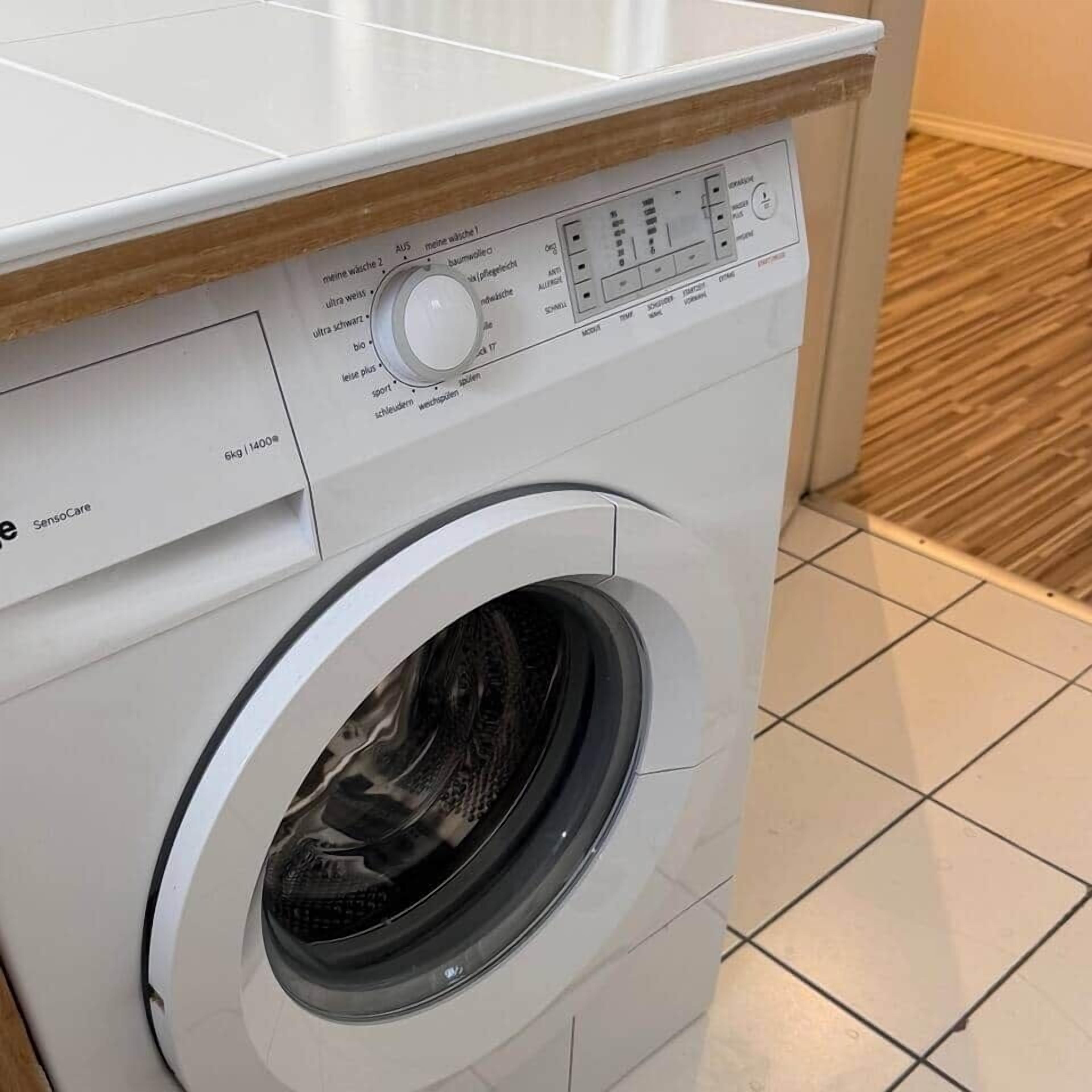 Voorweergave van een witte wasmachine met bedieningspaneel en een label met de tekst 'Sensocare'.