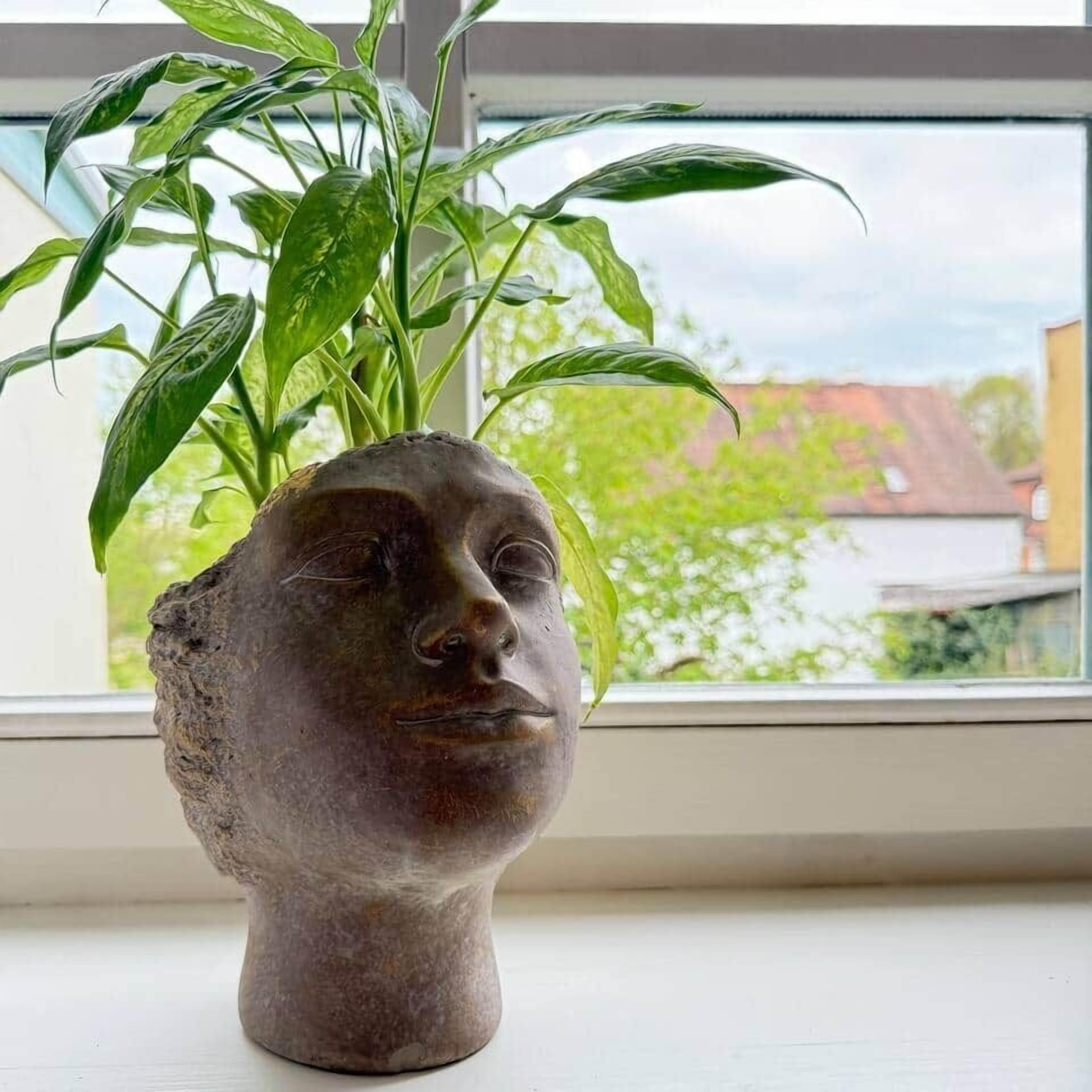 A potted plant with a stone sculpture base on a windowsill.