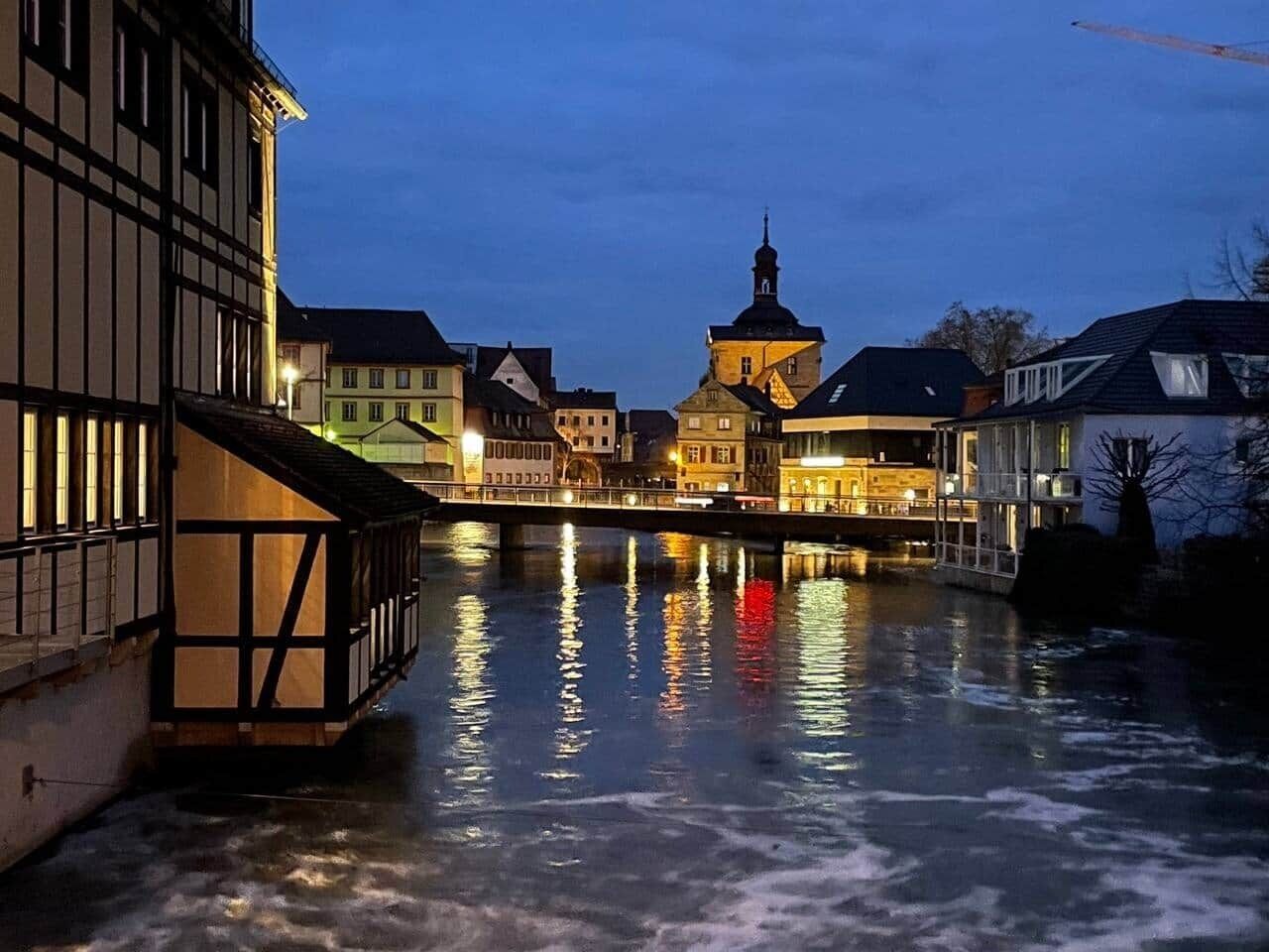 A nighttime view of a riverside town with buildings reflecting on the water.