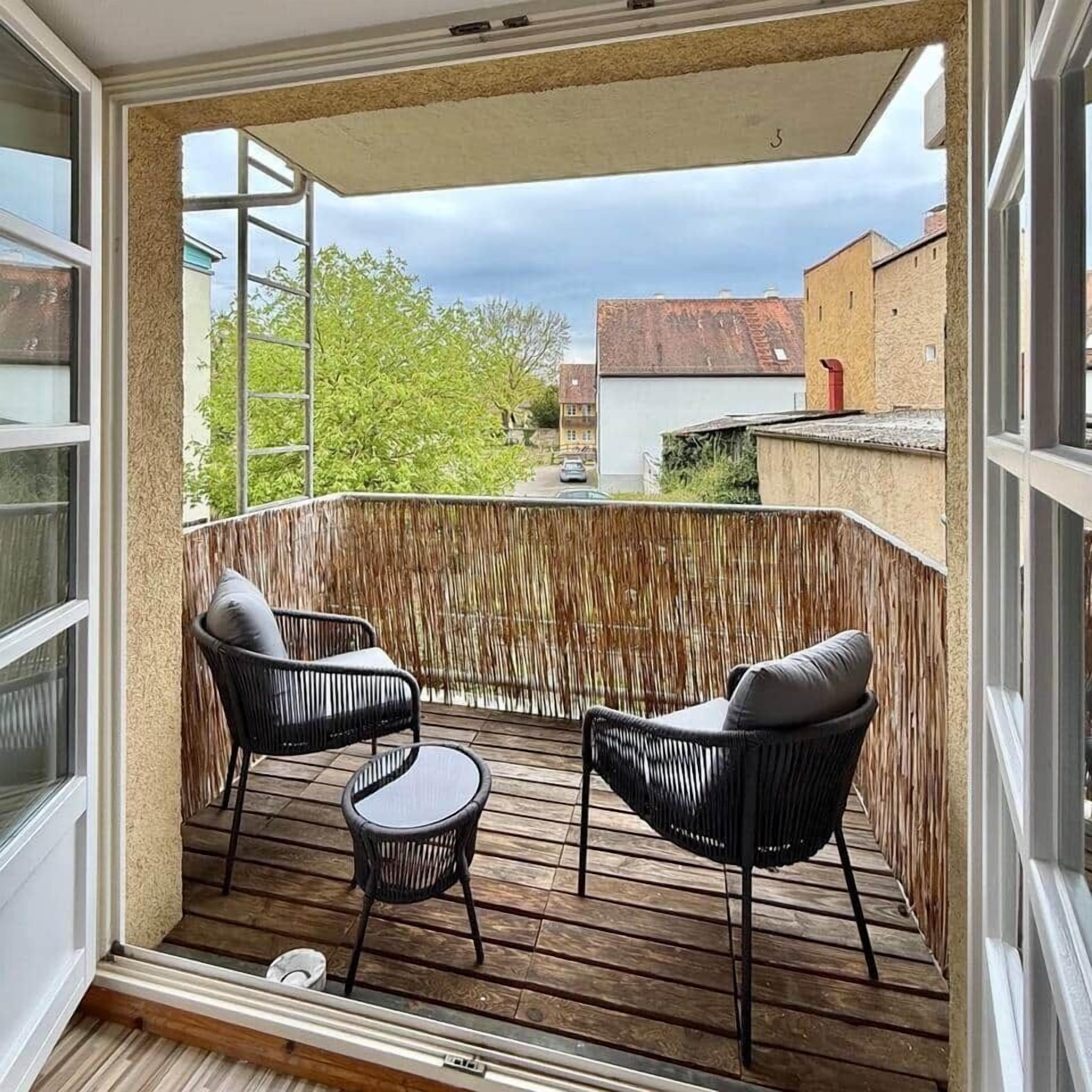 A balcony with two black wicker chairs and a small round table.