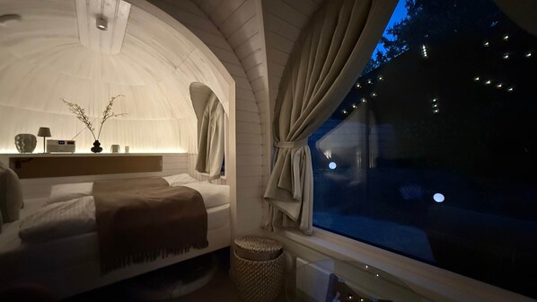 A cozy, arched bedroom with a bed, bedside table, lamp, and a view of the night sky. - Iglu – Chestnut (Frensdorf)