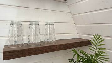 A corner with two wooden shelves against a white paneled wall, each holding clear glass cups and a potted plant.