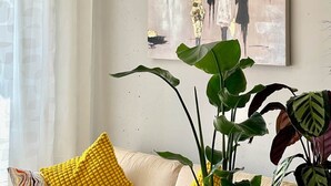 A living room with a beige sofa, a yellow cushion, and two potted plants. - Pretty City - Tiny Apartment Bamberg (Bamberg)