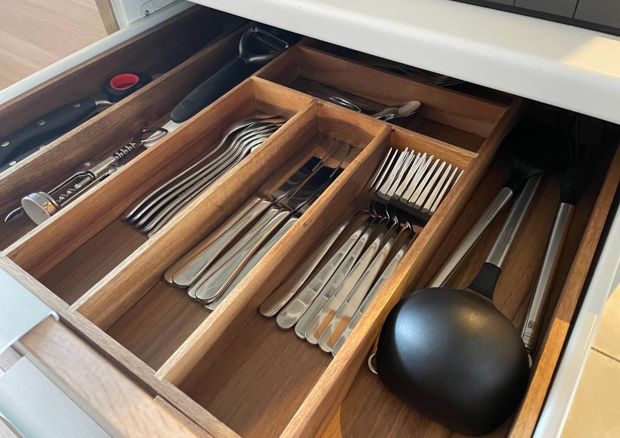 A drawer with multiple compartments containing various utensils like forks, knives, and spoons.