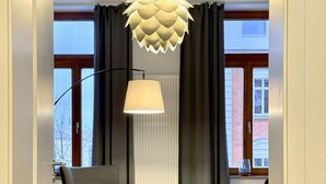 Un salon moderne avec un grand fauteuil, un petit pouf, une lampe sur pied et un luminaire au plafond original.