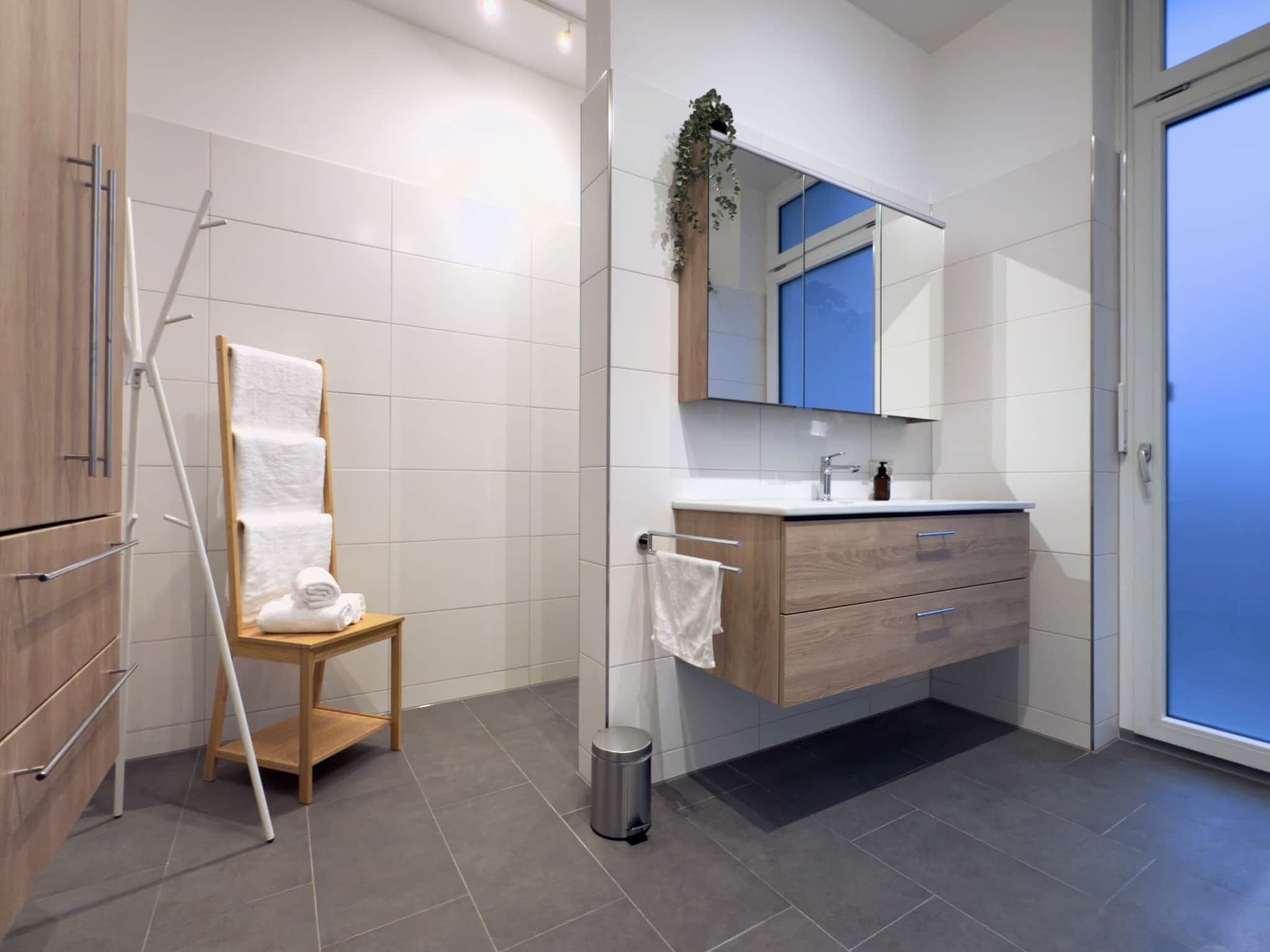 A modern bathroom with a wooden vanity, a mirror, and a towel rack.