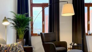 Un salon moderne comprenant un canapé, un fauteuil, un pouf, une lampe sur pied et une plante en pot.