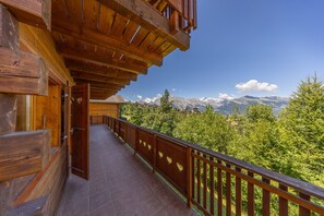 A wooden balcony with a view of snow-capped mountains and green trees.