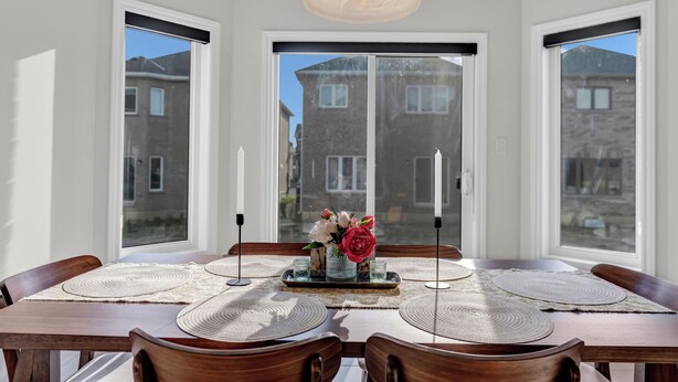 A dining area with a wooden table set for six, surrounded by chairs, with a decorative centerpiece and a hanging light fixture. - 100% Private and Spotless ~Fresh Linens ~New House (Thorold)