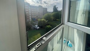 Vista dalla finestra su cielo sereno, un edificio a più piani e una zona verde con un'auto nelle vicinanze.