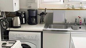 Una cucina compatta con lavatrice, fornello, macchina del caffè e lavandino.