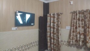 A room with a flat-screen TV mounted on the wall, a dark door, and patterned curtains. - Saraswat Niwas (Udaipur)