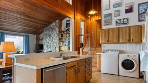 Uma cozinha compacta com armários de madeira, lava-louças embutida, máquina de lavar e parede decorada com pedra.
