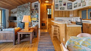 Interior acolhedor de uma cabana com parede de pedra, teto de madeira, área de cozinha e espaço de jantar.