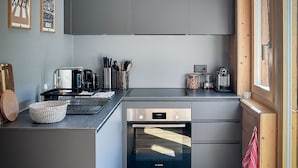 Et moderne køkken med grå skabe, en Bosch ovn og et vindue med træpersienner.