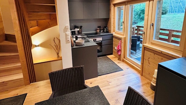 Et moderne køkken med mørke skabe, en central ø og et spiseområde med et bord og stole.