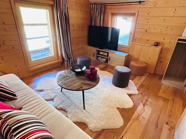 A cozy cabin interior with a wooden floor, a round table with candles, a sofa, and a flat-screen TV. - The Mazot - 4 Vallées Nendaz (Haute-Nendaz)