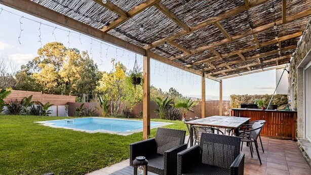 Un patio couvert avec une piscine, du mobilier d’extérieur et un mur en pierre.