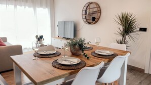 Un coin repas avec une table en bois dressée pour quatre personnes, des chaises blanches et un set de table en fibres tressées.
