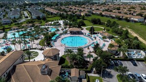 An aerial view of a resort with multiple swimming pools, a central circular pool, and surrounding lounge areas.