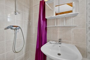 A bathroom with a shower, a sink, a mirror, and a purple shower curtain.