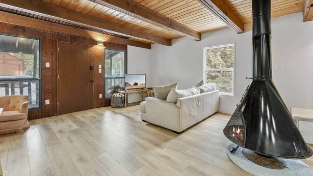 A spacious living room with a fireplace, wooden ceiling beams, and large windows.