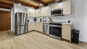 A modern kitchen with stainless steel appliances, wooden cabinets, and a wooden ceiling.
