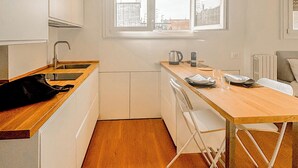 Una cocina moderna con armarios blancos, encimera de madera, una mesa de comedor con sillas y una ventana con vistas a edificios.