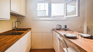 Una cocina compacta con armarios blancos, una encimera de madera, un ventanal y una silla blanca.