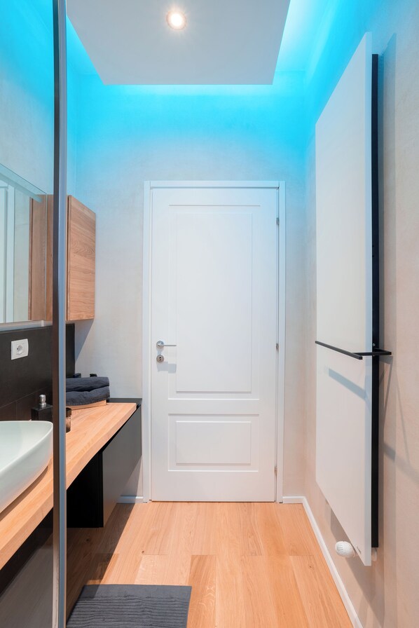 Un baño moderno con cabina de ducha de vidrio, una puerta blanca y un tocador de madera.