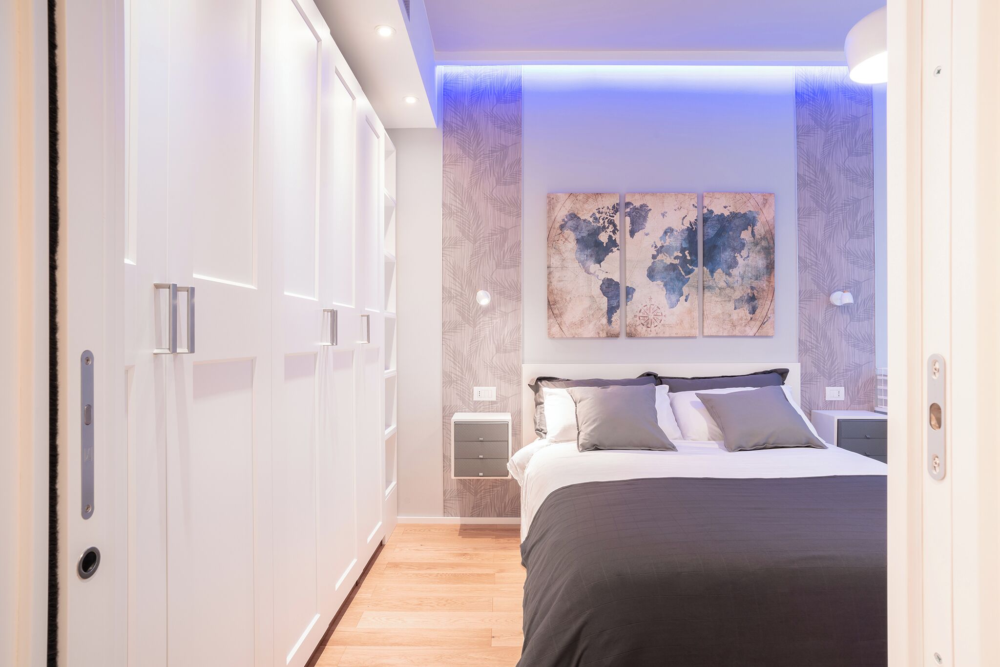 A modern bedroom with a large bed, a wardrobe, and a world map artwork on the wall.
