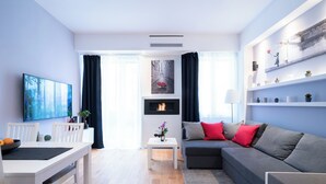 Ein modernes Wohnzimmer mit Essbereich, einem grauen Sofa, einem Flachbildfernseher und einem Kamin.