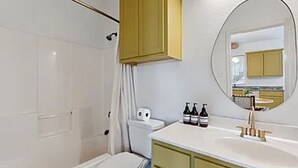 Une salle de bain avec des toilettes, une douche, un lavabo avec des bouteilles et un miroir.